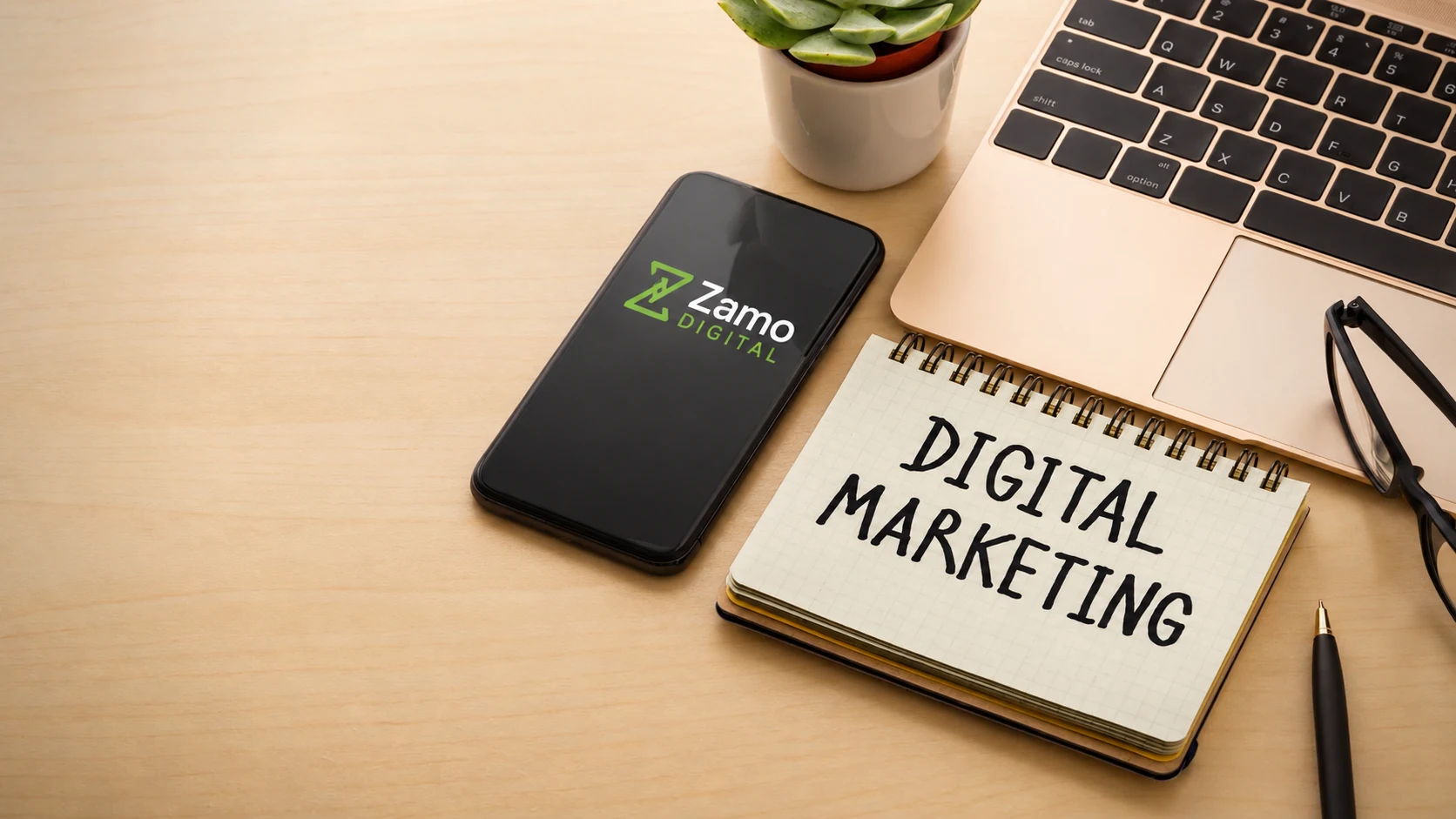 Bureau avec un téléphone au logo Zamo Digital, un ordinateur et un carnet de marketing numérique